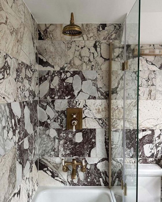 Bathroom setting featuring Fitzrovia Viola 30.5x61cm natural marble tiles with a honed finish, showcasing a white base with bold burgundy and deep grey veining, paired with brass fittings for a rich, statement finish.