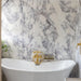 Bathroom interior featuring Fitzrovia Lilac 30.5 x 61cm honed natural marble tiles across walls and floor, showcasing soft lilac veining against a light base, styled with a freestanding bath, brushed brass fittings, and a bright, refined setting.