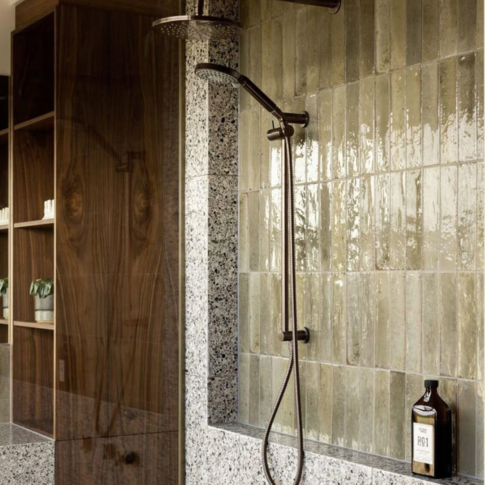 Bathroom featuring Izmir Sage Green gloss brick tiles in a 6 × 25cm ceramic format, installed vertically to create a soft, elongated look, with subtle tonal variation and a high-gloss finish that reflects natural light, paired with warm wood panelling, terrazzo surfaces and minimalist brass fittings for a calm, spa-inspired interior.
