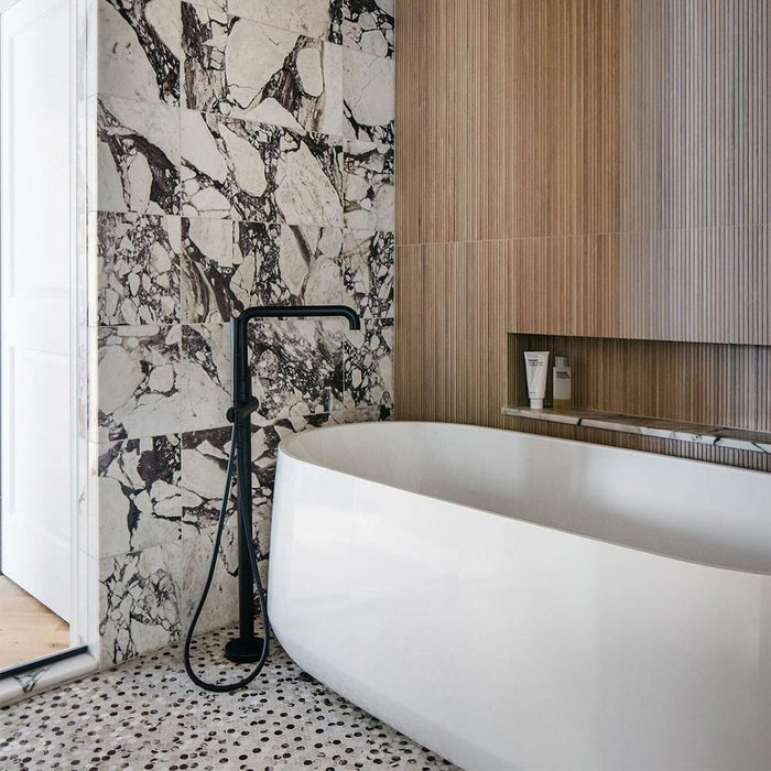 Bathroom setting featuring Fitzrovia Viola 30.5x61cm natural marble tiles with a honed finish, showcasing a white base with striking burgundy and deep grey veining, paired with warm wood textures and matte black fittings for a contemporary, design-led contrast.