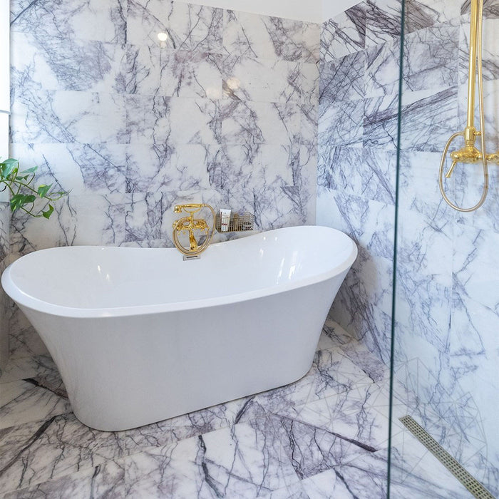 Bathroom interior featuring Fitzrovia Lilac 30.5 x 61cm honed natural marble tiles across walls and floor, showcasing soft lilac veining against a light base, styled with a freestanding bath, brushed brass fittings, and a bright, refined setting.