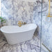 Bathroom interior featuring Fitzrovia Lilac 30.5 x 61cm honed natural marble tiles across walls and floor, showcasing soft lilac veining against a light base, styled with a freestanding bath, brushed brass fittings, and a bright, refined setting.