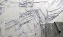 Bathroom wall detail featuring Fitzrovia Lilac 30.5 x 61cm honed natural marble tiles, showcasing soft white tones with flowing lilac-grey veining, styled with a chrome towel rail and textured grey towel for a calm, contemporary finish.