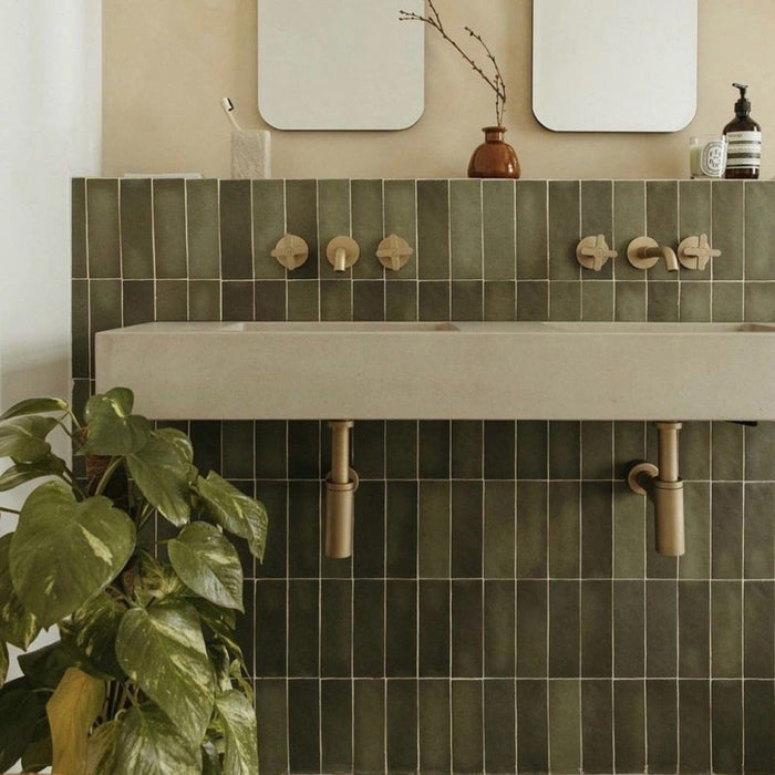 Bathroom interior featuring Atlas Verde Mini Brick Matt tiles in 5cm x 15cm format, showcasing deep green tones with subtle variation, laid vertically behind a wall-mounted basin with brushed brass fittings.