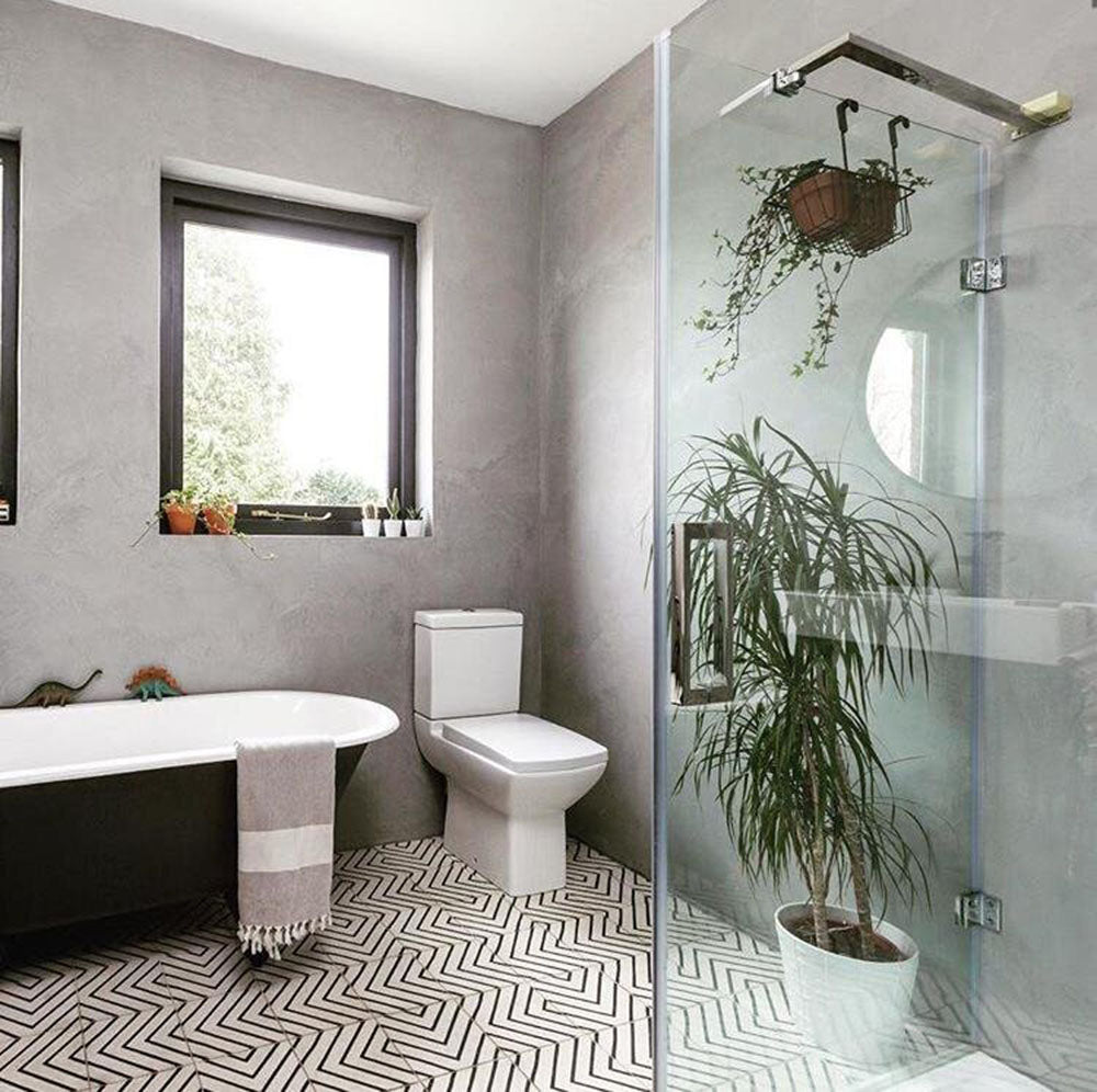 Alhambra Zig Zag Blanco 20x20cm Moroccan tiles used in a modern bathroom with grey walls, a freestanding bath, glass shower, and potted plants, highlighting the bold black and white geometric zig-zag pattern on the floor.