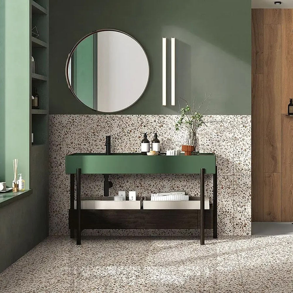 Bathroom featuring Dino Terrazzo Blanco Drops 20x20cm terrazzo-style ceramic wall and floor tiles, styled with a green vanity unit, round mirror, and wooden wall accents.