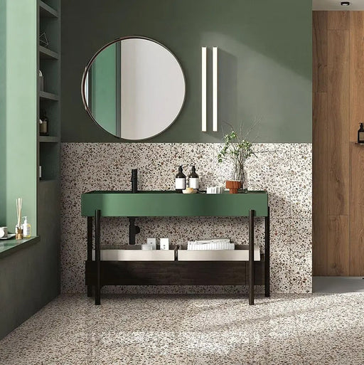 Bathroom featuring Dino Terrazzo Blanco Drops 20x20cm terrazzo-style ceramic wall and floor tiles, styled with a green vanity unit, round mirror, and wooden wall accents.