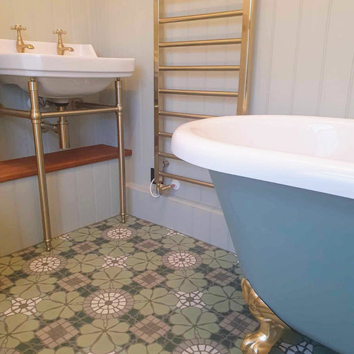 Bathroom featuring Bloom Green 20x20cm Moroccan-style ceramic floor tiles with green, white, and grey floral patterns, styled with a freestanding blue clawfoot bath, brass fixtures, and a white sink with gold taps.