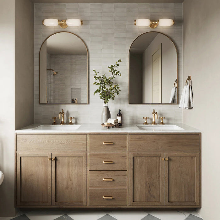 Bathroom setting featuring Atlas White Mini Brick 5x15cm matt wall tiles, laid in a horizontal brick format to create a soft, textured backdrop. The subtle tonal variation and refined matt finish bring a calm, understated feel, paired with warm wood cabinetry, brass fittings, and arched mirrors for a balanced, contemporary look.