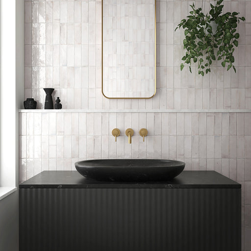 Bathroom interior featuring Beijing White 5.1x16.1cm Moroccan brick tiles laid vertically on the wall, paired with brushed brass fixtures, a black countertop basin, and a gold-framed mirror for a modern minimalist look.