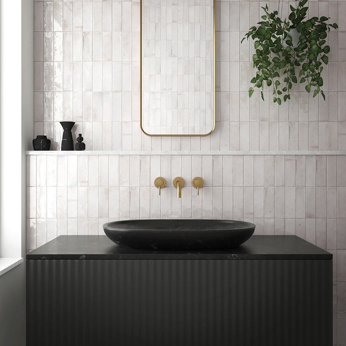 Bathroom interior featuring Beijing White 5.1x16.1cm Moroccan brick tiles laid vertically on the wall, paired with brushed brass fixtures, a black countertop basin, and a gold-framed mirror for a modern minimalist look.