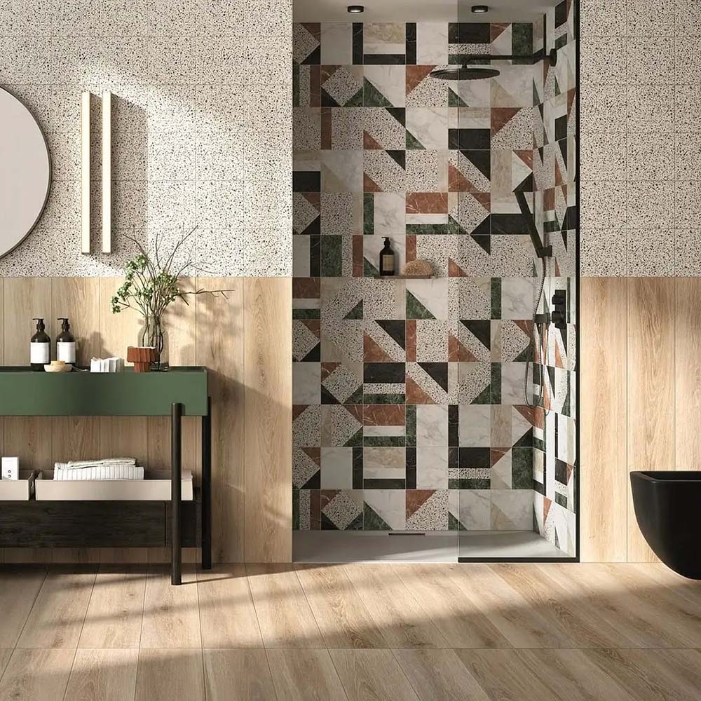 Bathroom featuring Dino Terrazzo Blanco Decor 20x20cm terrazzo-style ceramic wall tiles, styled with light wood panelling, a green vanity unit, and a geometric shower design.