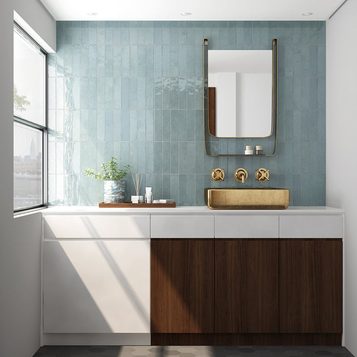 Madison Aquamarine Brick Wall Tiles 6x24.6cm — showcased in a serene bathroom setting, these glossy teal tiles create a refreshing spa-like atmosphere. Their handmade appearance adds character and depth, beautifully offset by brass accents and warm wood cabinetry for a luxurious modern finish.