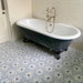 Maroush Frost Blue 18.7x21.6cm Moroccan hexagonal tiles with a soft blue and white floral geometric pattern, used as a bathroom floor beneath a freestanding clawfoot bathtub and light cabinetry.