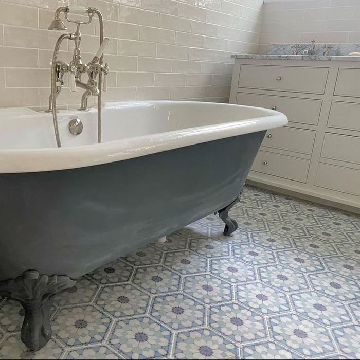 Maroush Frost Blue 18.7x21.6cm Moroccan hexagonal tiles with a soft blue and white floral geometric pattern, used as a bathroom floor beneath a freestanding clawfoot bathtub and light cabinetry.