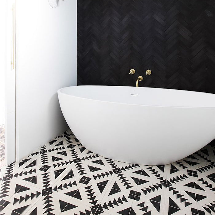 Alhambra Alkazar 20x20cm Moroccan tiles used on a bathroom floor, featuring striking black and white geometric patterns that complement the matte black herringbone wall and freestanding white bathtub with brass fittings.