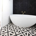 Alhambra Alkazar 20x20cm Moroccan tiles used on a bathroom floor, featuring striking black and white geometric patterns that complement the matte black herringbone wall and freestanding white bathtub with brass fittings.