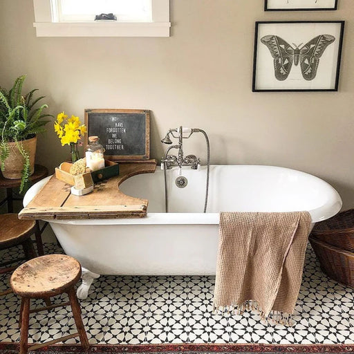Bathroom featuring Agraba Black and White Mini 15x15cm Moroccan-style ceramic floor tiles, styled with a freestanding white roll-top bath, rustic wooden accents, and neutral décor for a vintage-inspired look.