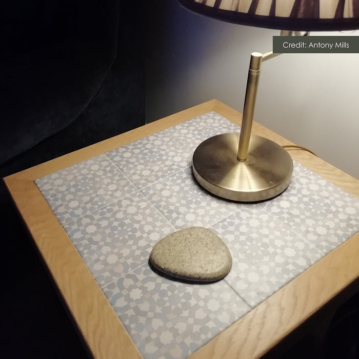 Close-up of Bedouin Tetuan Blue 15cm x 15cm Moroccan style tiles used to decorate a wooden side table, featuring an intricate blue and white geometric pattern alongside a brass lamp.