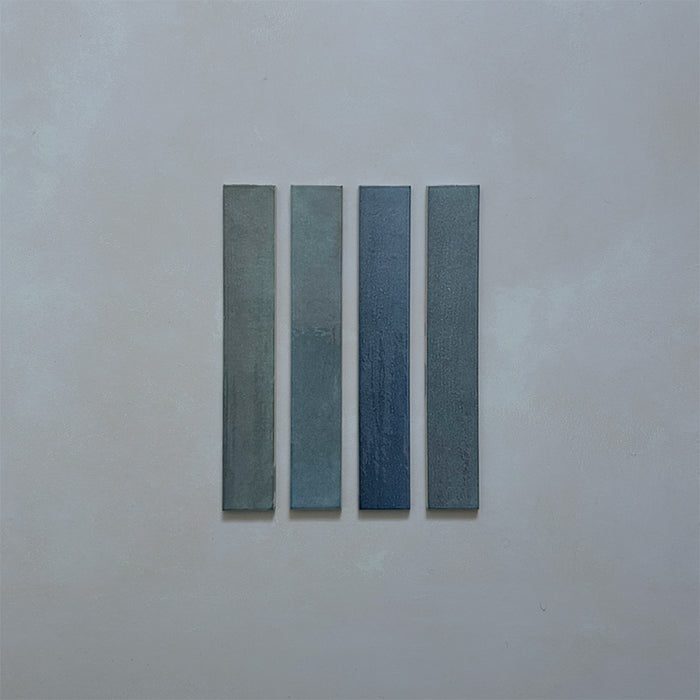 Close-up of Belem Blue 5cm x 30cm artisanal porcelain wall tiles, displaying four slim brick tiles with varied blue and blue-green tones, subtle texture and gentle tonal variation.