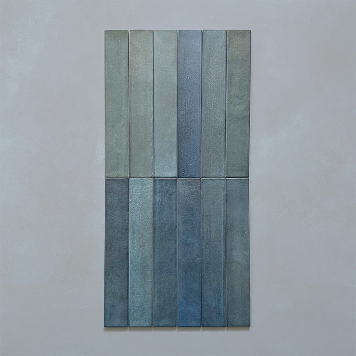 Close-up of Belem Blue 5cm x 30cm artisanal porcelain wall tiles, showcasing the slim brick format, soft blue and blue-green tones, subtle surface texture and varied tonal finish.