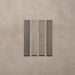 Close-up of Belem Grey 5cm x 30cm artisanal porcelain wall tiles, displaying four slim brick tiles with varied grey and taupe tones, subtle texture and gentle tonal variation.
