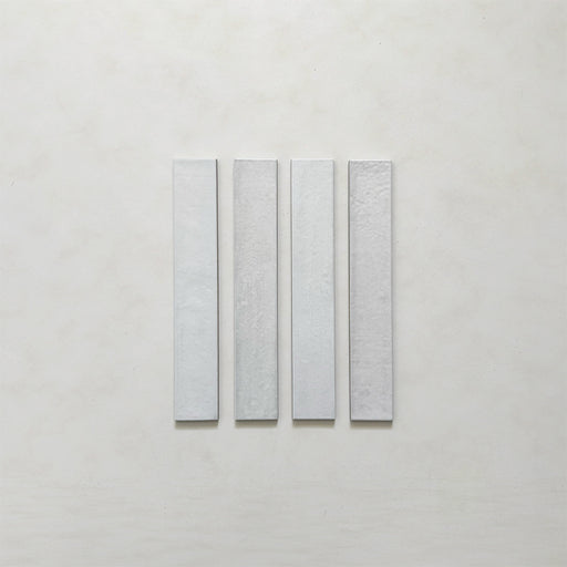 Close-up of four Belem White 5cm x 30cm artisanal porcelain wall tiles, showcasing the slim brick format, soft white colouring and subtle surface texture and tonal variation.