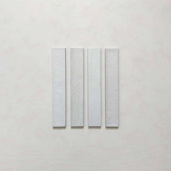 Close-up of four Belem White 5cm x 30cm artisanal porcelain wall tiles, showcasing the slim brick format, soft white colouring and subtle surface texture and tonal variation.