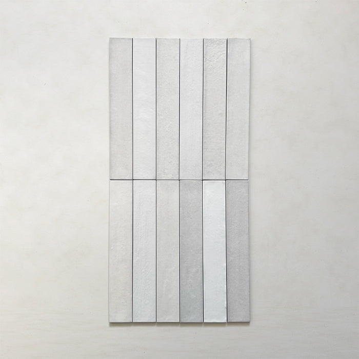 Close-up of Belem White 5cm x 30cm artisanal porcelain wall tiles arranged vertically, showcasing soft white tones, subtle tonal variation and a gently textured handcrafted-effect surface finish.