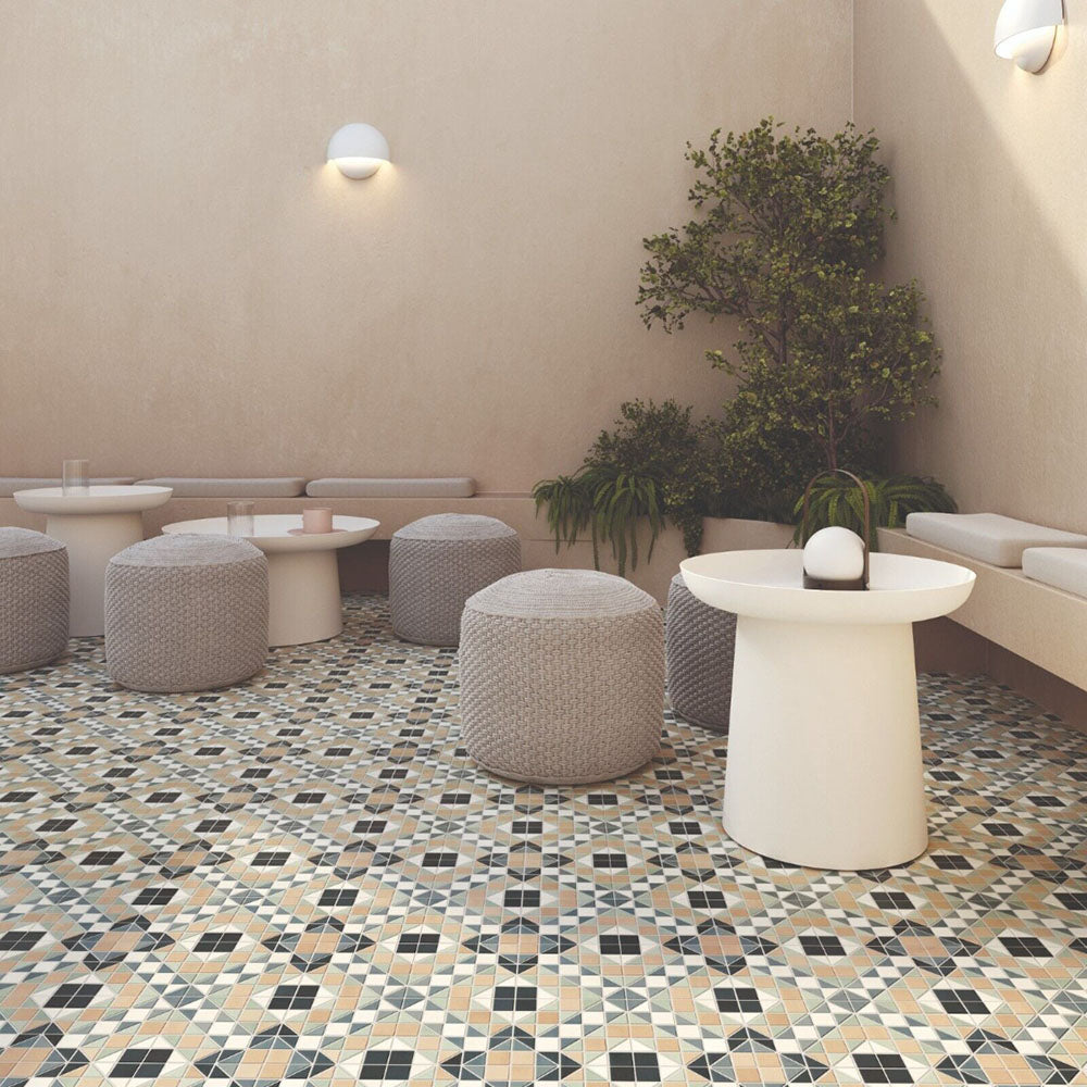 Outdoor seating area featuring Belgravia Marina Plus Mosaic 28 × 28cm Victorian style patterned floor tiles, with intricate geometric detailing in soft blue, green and beige tones, paired with neutral seating, textured pouffes, and warm-toned walls.