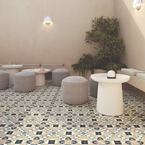 Outdoor seating area featuring Belgravia Marina Plus Mosaic 28 × 28cm Victorian style patterned floor tiles, with intricate geometric detailing in soft blue, green and beige tones, paired with neutral seating, textured pouffes, and warm-toned walls.
