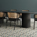 Dining area featuring Belgravia Marina Plus Mosaic 28 × 28cm Victorian style patterned floor tiles, with intricate geometric detailing in muted blue, green and beige tones, paired with a dark wood table, woven chairs, and deep green walls.