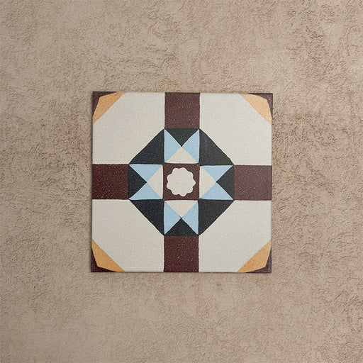 Single Europa Berlin 20x20cm Victorian Moroccan style tile displayed against a textured beige background, featuring a geometric star pattern in burgundy, blue, mustard and cream tones in a close-up product setting.