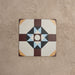 Single Europa Berlin 20x20cm Victorian Moroccan style tile displayed against a textured beige background, featuring a geometric star pattern in burgundy, blue, mustard and cream tones in a close-up product setting.