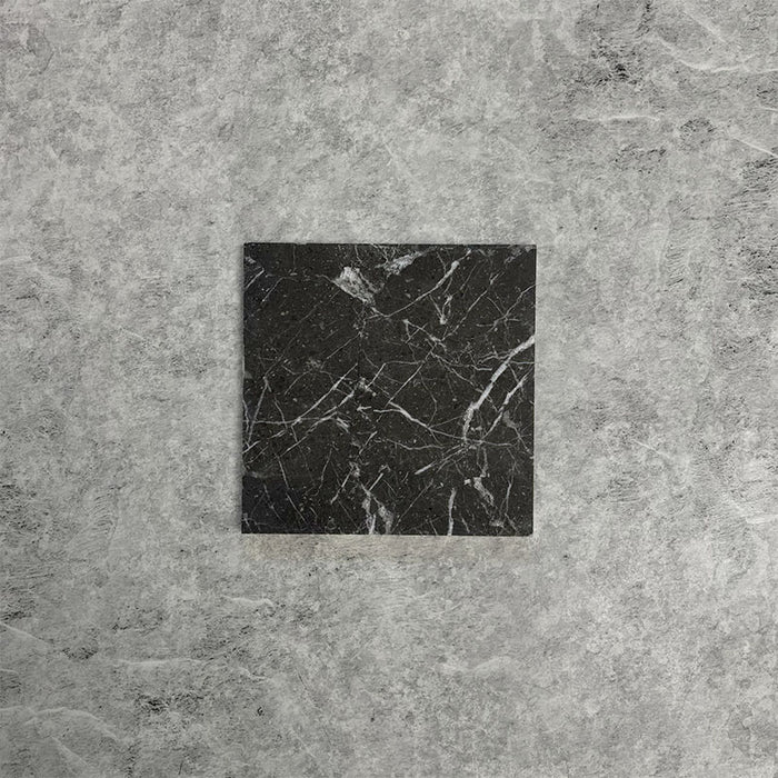 Single Fitzrovia Black 15.2x15.2cm honed natural marble tile displayed on a neutral grey surface, showcasing deep black tones, striking white veining, and a smooth, refined finish.