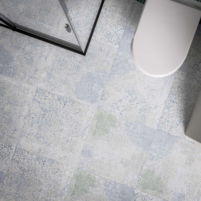 Bathroom floor featuring Boheme Blue Patterned 59.55cm x 59.55cm tiles, showcasing a soft patchwork design in blue, grey and subtle green tones, paired with a black framed shower enclosure and white bathroom fixtures.