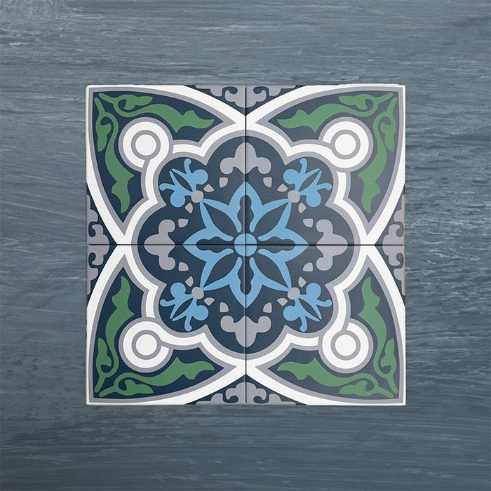 Four Europa Bucharest 20x20cm Victorian Moroccan style tiles arranged together to showcase the repeating ornamental pattern in blue, green, grey and white tones, displayed against a textured blue background.