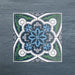 Four Europa Bucharest 20x20cm Victorian Moroccan style tiles arranged together to showcase the repeating ornamental pattern in blue, green, grey and white tones, displayed against a textured blue background.