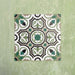 Four Europa Budapest 20x20cm Victorian Moroccan style tiles displayed together against a textured green wall, forming a symmetrical geometric pattern in green, cream, black and taupe tones in a styled product setting.