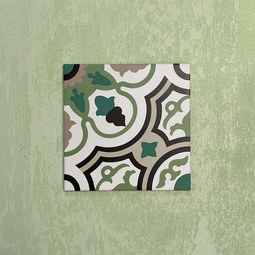 Single Europa Budapest 20x20cm Victorian Moroccan style tile displayed against a textured green wall, showcasing an intricate geometric pattern in green, cream, black and taupe tones in a close-up product setting.