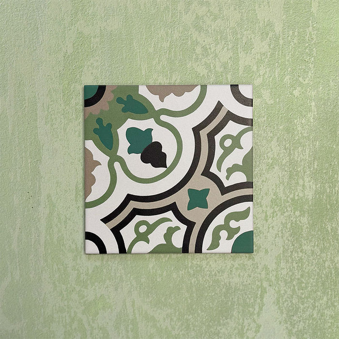 Single Europa Budapest 20x20cm Victorian Moroccan style tile displayed against a textured green wall, showcasing an intricate geometric pattern in green, cream, black and taupe tones in a close-up product setting.