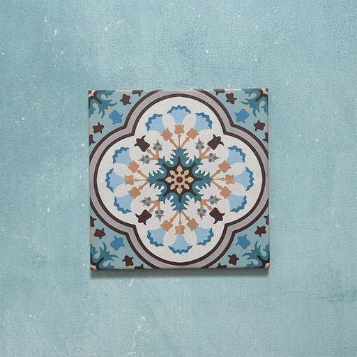 Cabana Bayamo Moroccan style patterned tile in a 20cm x 20cm format, featuring an intricate geometric floral design in soft blue, cream, teal and warm brown tones, shown against a textured blue background.