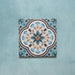 Cabana Bayamo Moroccan style patterned tile in a 20cm x 20cm format, featuring an intricate geometric floral design in soft blue, cream, teal and warm brown tones, shown against a textured blue background.