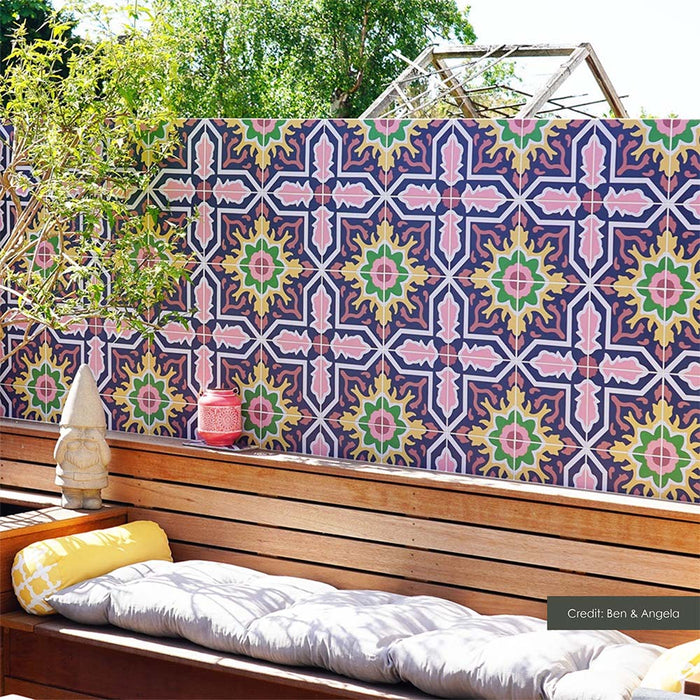 Outdoor seating area featuring Cabana Havana 20x20cm Moroccan-style patterned wall tiles, with vibrant navy blue, pink, green and yellow geometric floral motifs, creating a colourful backdrop behind a wooden bench with cushions.