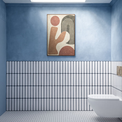 Chemistry White 6.5cm x 30cm wall tiles installed vertically across the lower half of a modern bathroom wall, featuring a crisp white finish with contrasting dark blue edges, paired with soft blue walls and a white wall-mounted toilet.