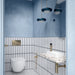 Chemistry White 6.5cm x 30cm wall tiles installed vertically around a contemporary bathroom, featuring a white finish with contrasting dark blue edges, paired with soft blue walls, brushed brass fittings and a terrazzo effect vanity top.