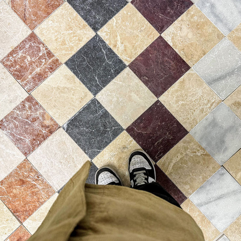 Top-down view of Fitzrovia Cappuccino 15.2x15.2cm tumbled natural marble tiles within a multi-tone chequerboard floor, showcasing warm beige tones, natural veining, and varied marble colours in a classic patterned layout.