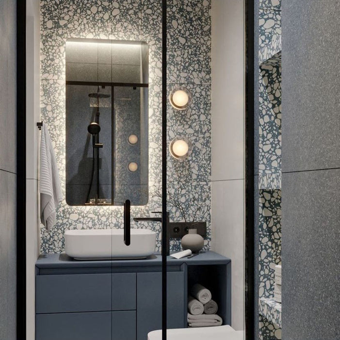 Modern bathroom featuring Chunks Pop Blue 60cm x 120cm terrazzo effect porcelain feature wall tiles, paired with large-format grey wall tiles, a blue floating vanity, black brassware and illuminated mirror.