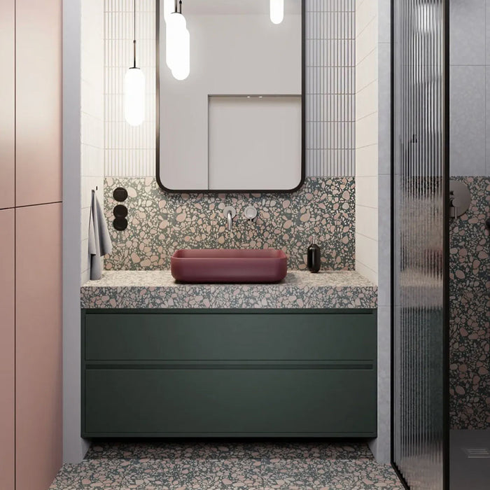 Modern bathroom featuring Chunks POP Terrazzo Green 60 × 120cm terrazzo-effect porcelain wall and floor tiles, paired with deep green cabinetry, a burgundy basin, ribbed glass shower screen, and soft contemporary lighting.