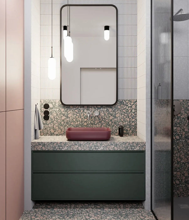 Modern bathroom featuring Chunks POP Terrazzo Green 60 × 120cm terrazzo-effect porcelain wall and floor tiles, paired with deep green cabinetry, a burgundy basin, ribbed glass shower screen, and soft contemporary lighting.